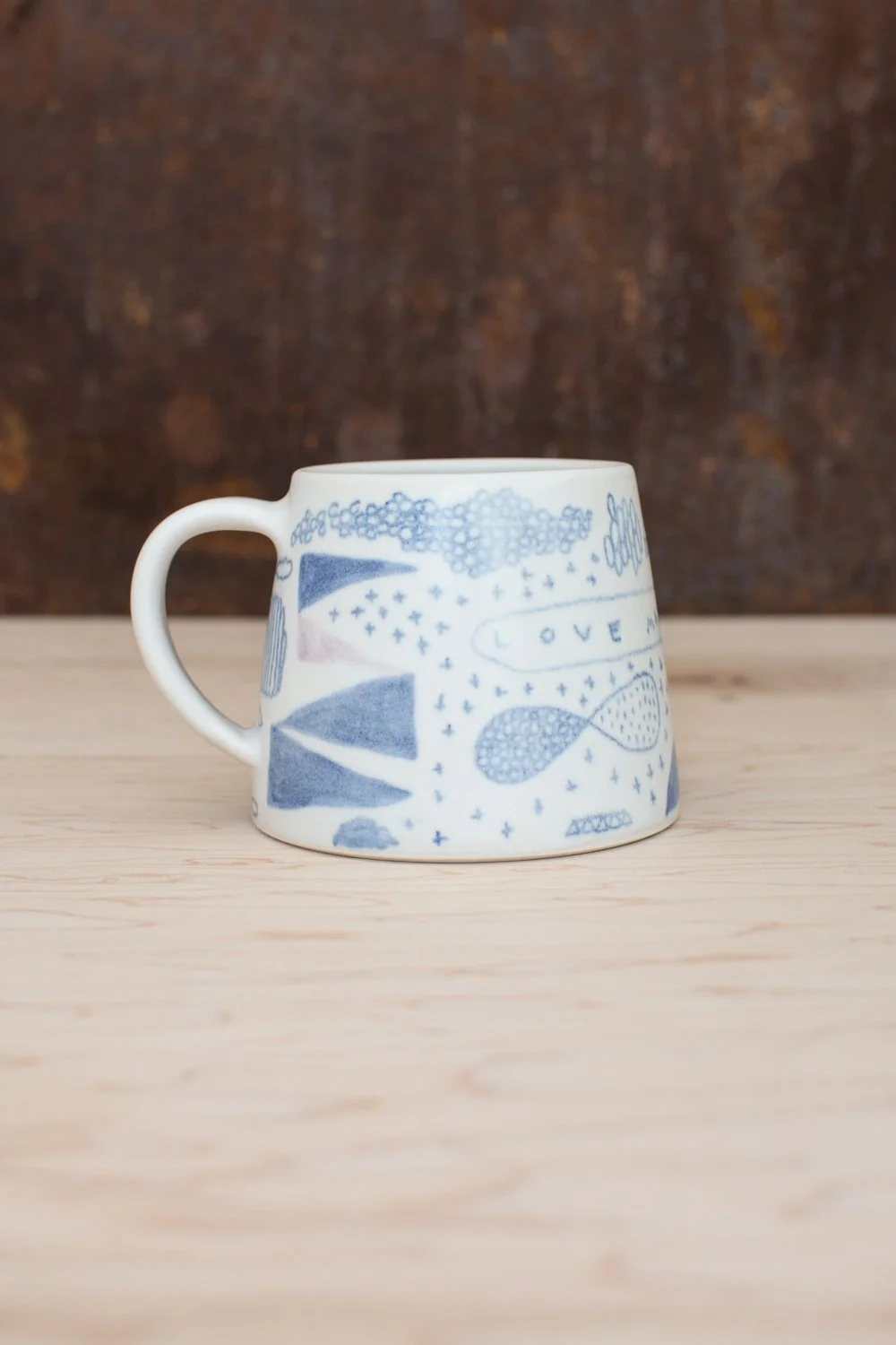 Hand-thrown porcelain mug with blue and pink illustrations.