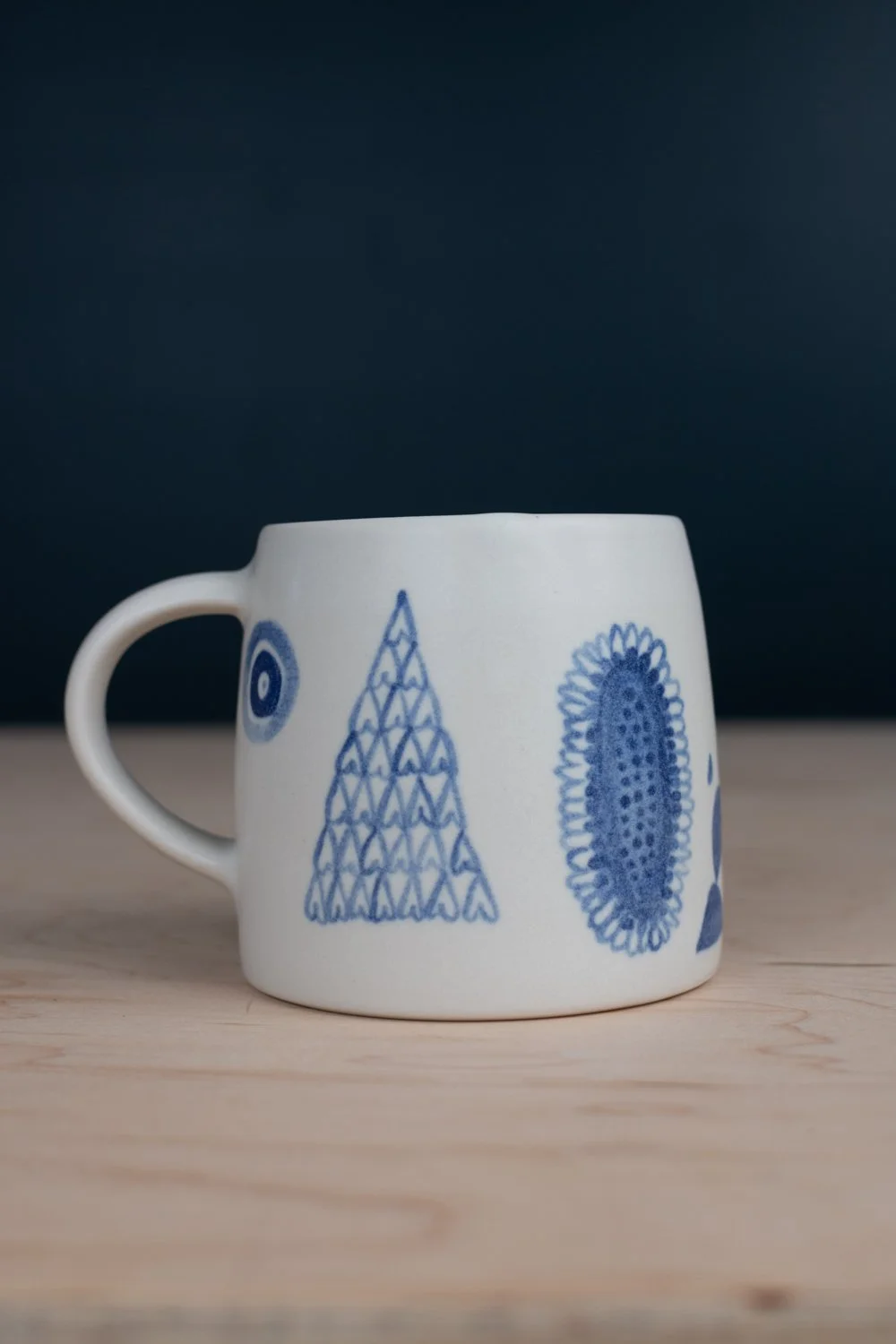 Hand-thrown porcelain mug with blue illustrations painted on the surface.