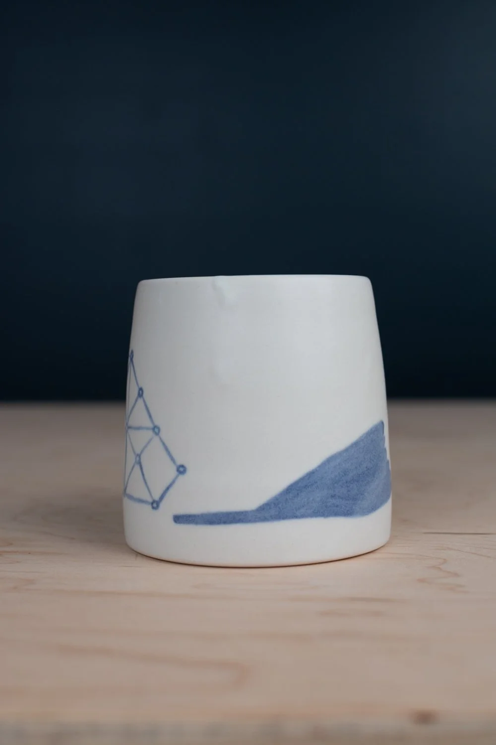 Hand-thrown porcelain mug with blue illustrations painted on the surface.