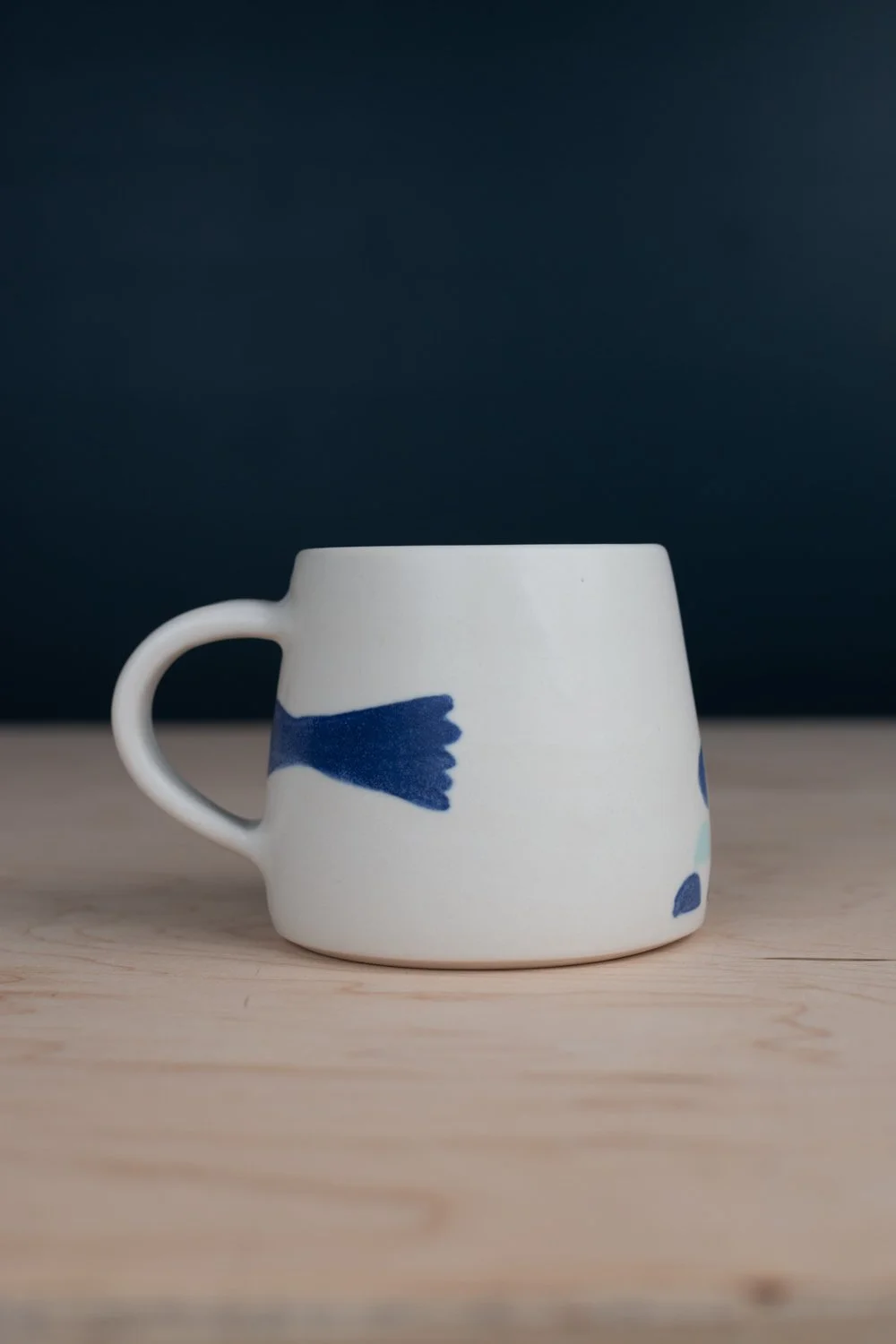 Hand-thrown porcelain mug with blue illustrations painted on the surface.