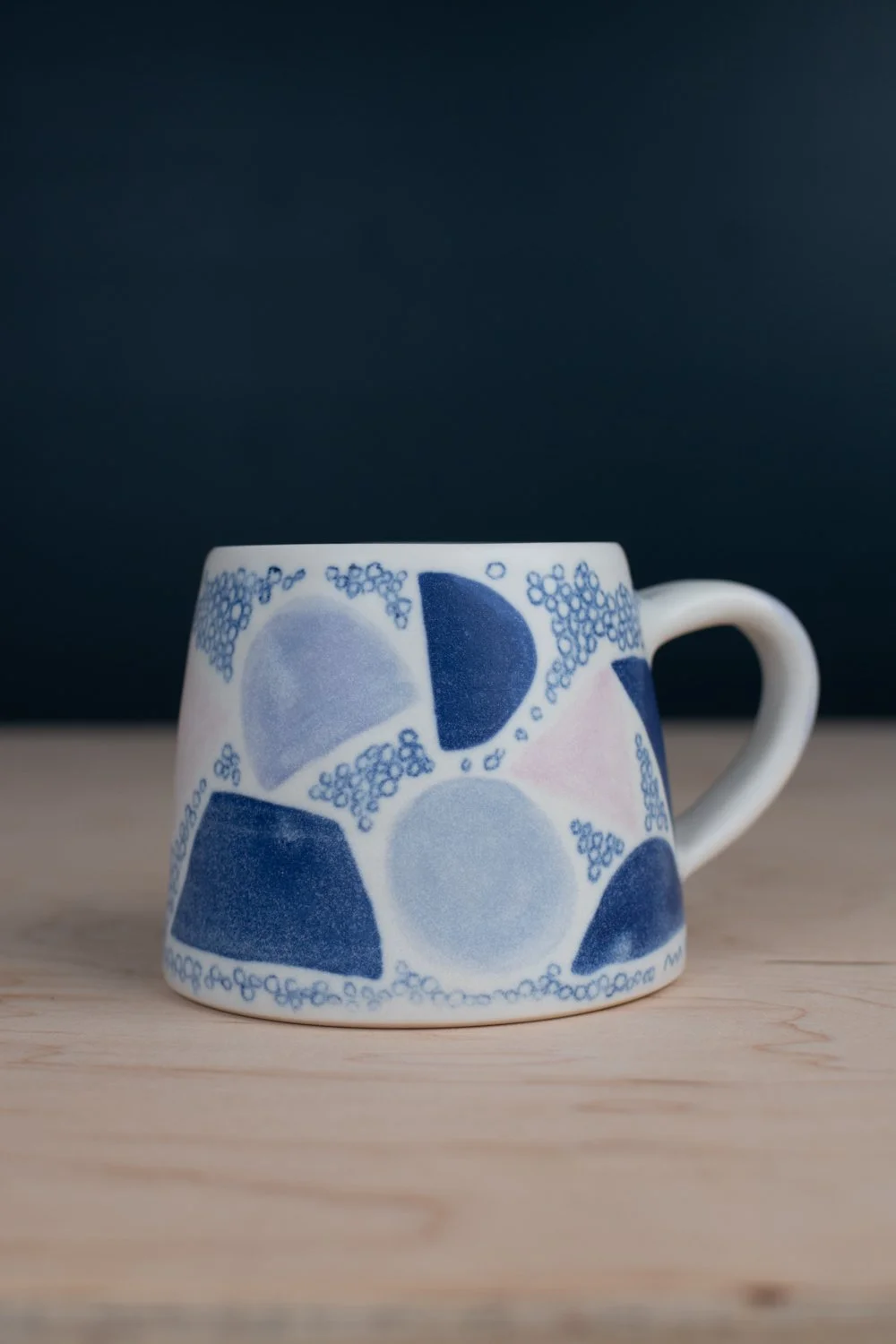 Hand-thrown porcelain mug with blue illustrations painted on the surface.