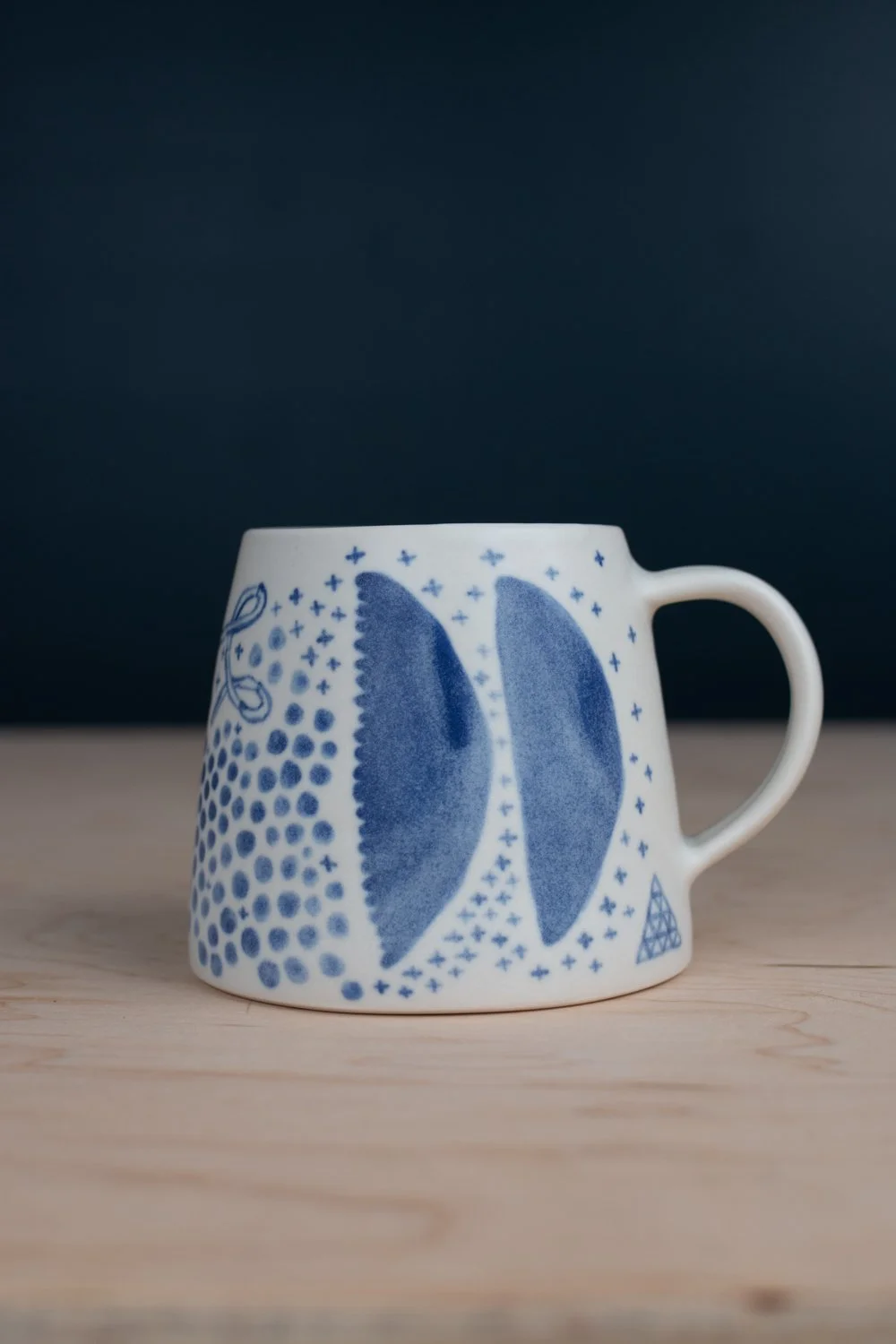 Hand-thrown porcelain mug with blue illustrations painted on the surface.