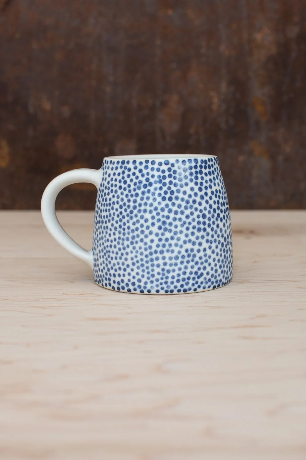 Hand-thrown porcelain mug with blue dots painted on the surface.