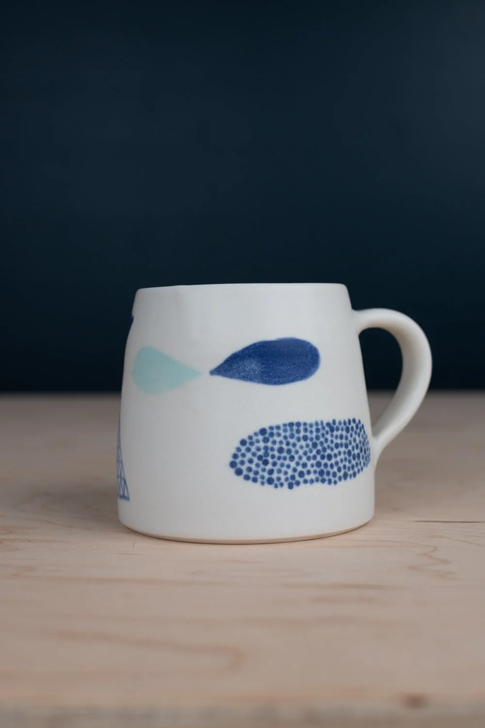 Hand-thrown porcelain mug with blue illustrations painted on the surface.