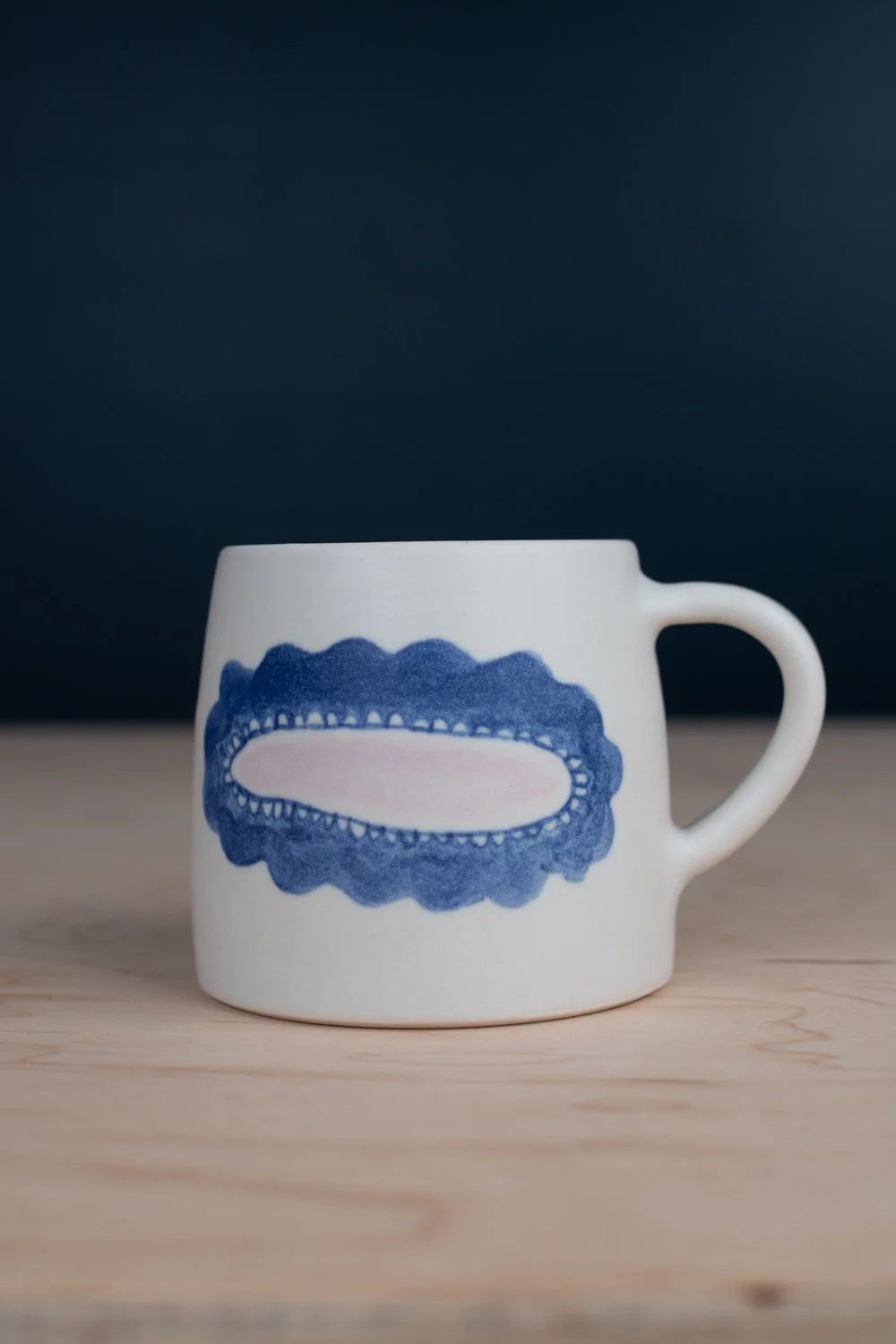 Hand-thrown porcelain mug with blue illustrations painted on the surface.