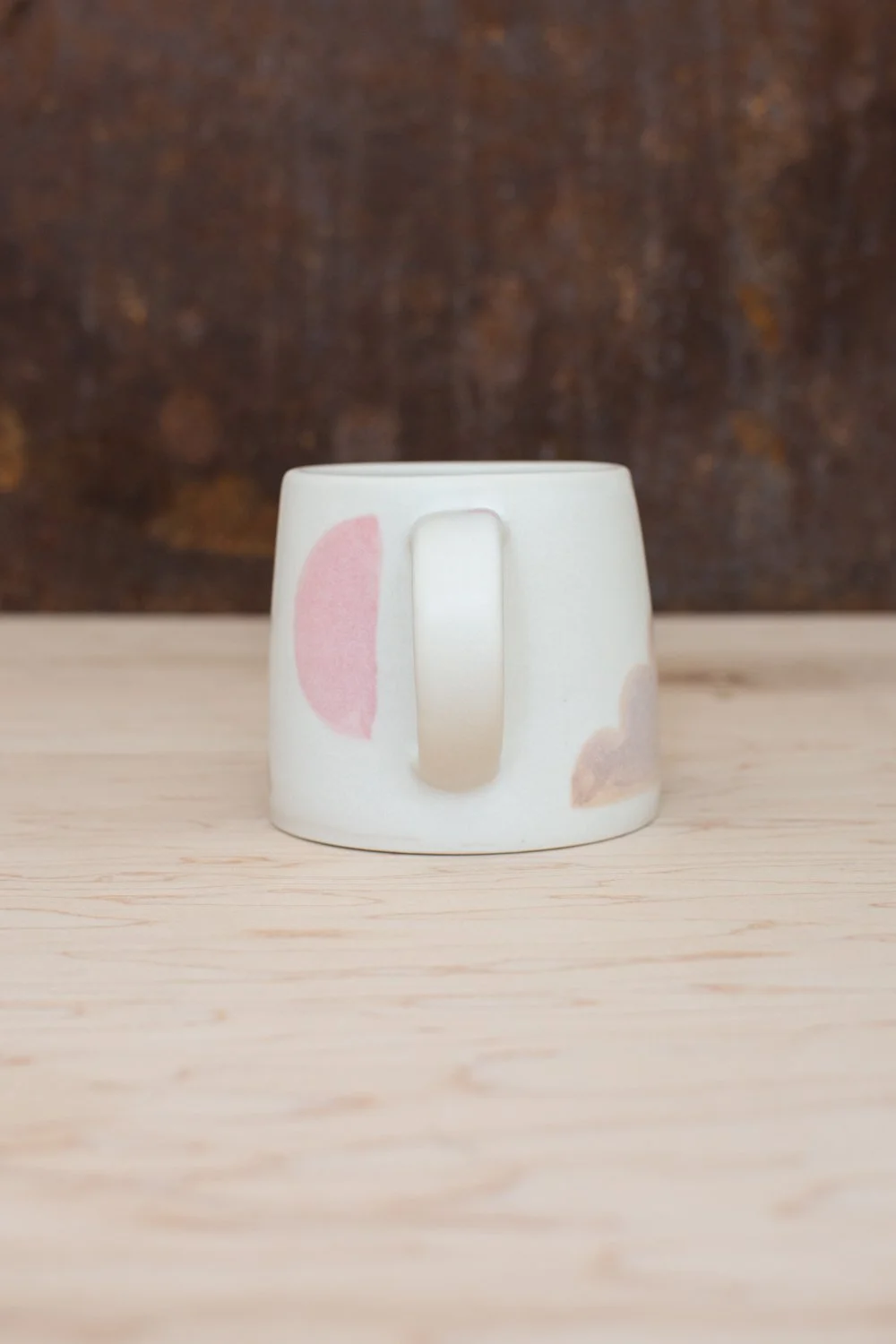 Hand-thrown porcelain mug with pink and ochre illustrations painted on the surface.