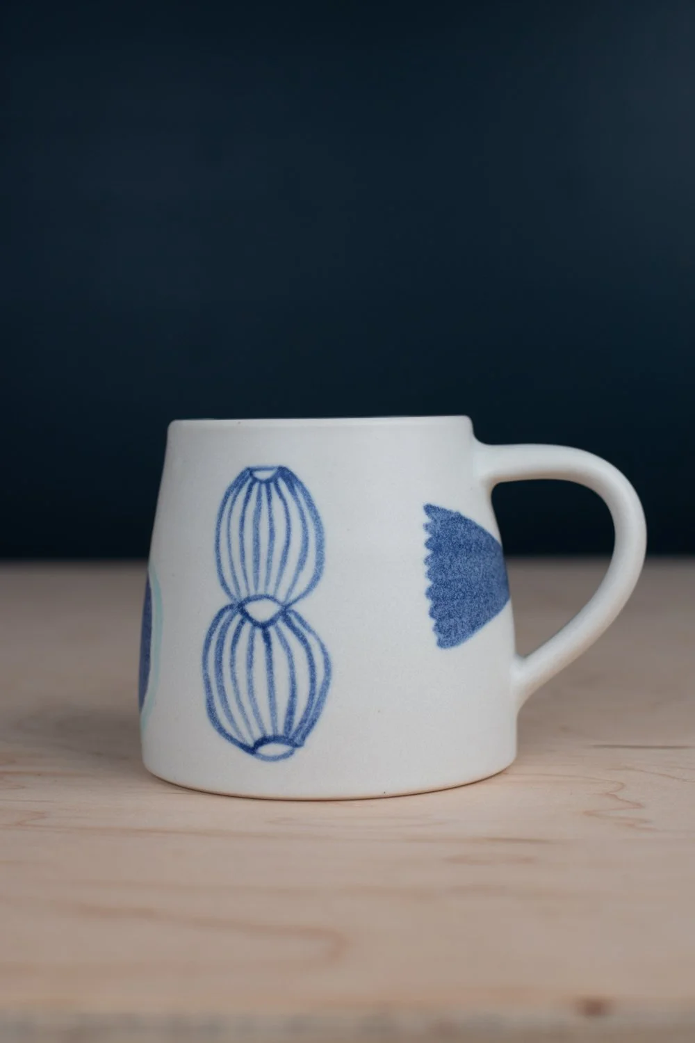 Hand-thrown porcelain mug with blue illustrations painted on the surface.