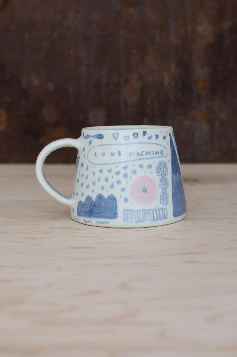 Hand-thrown porcelain mug with blue illustrations painted on the surface.