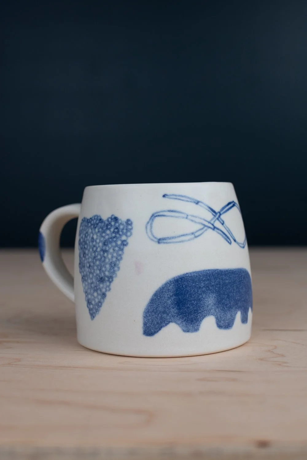 Hand-thrown porcelain mug with blue illustrations painted on the surface.