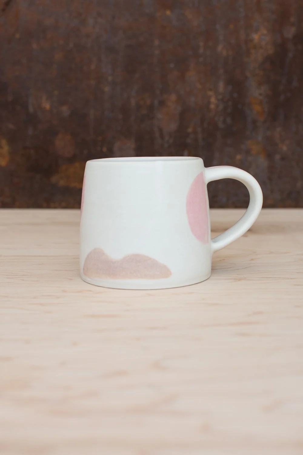 Hand-thrown porcelain mug with pink and ochre illustrations painted on the surface.