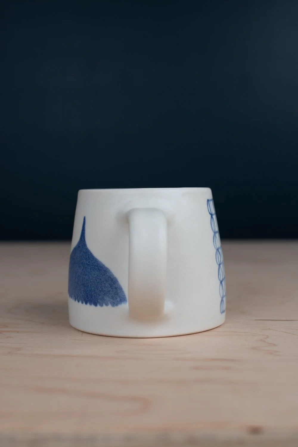 Hand-thrown porcelain mug with blue illustrations painted on the surface.