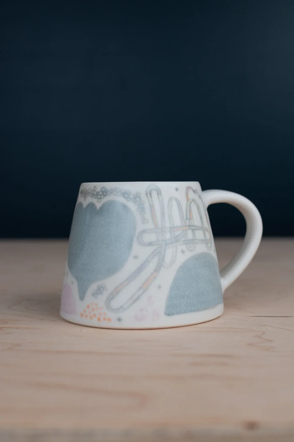Hand-thrown porcelain mug with green, yellow, and lilac illustrations painted on the surface.