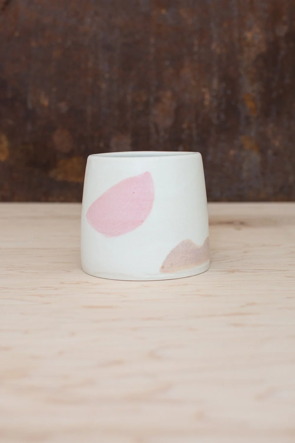 Hand-thrown porcelain mug with pink and ochre illustrations painted on the surface.
