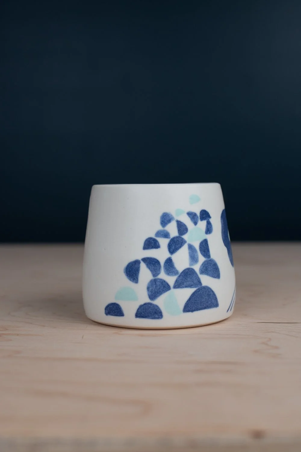 Hand-thrown porcelain mug with blue illustrations painted on the surface.