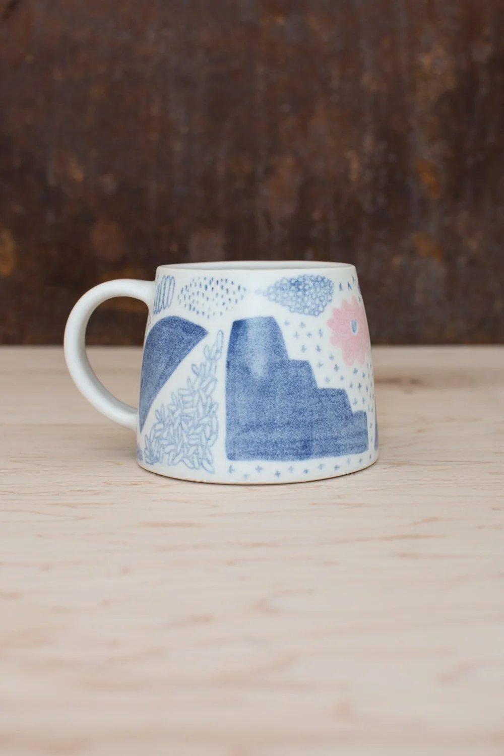 Hand-thrown porcelain mug with blue and pink illustrations painted on the surface.