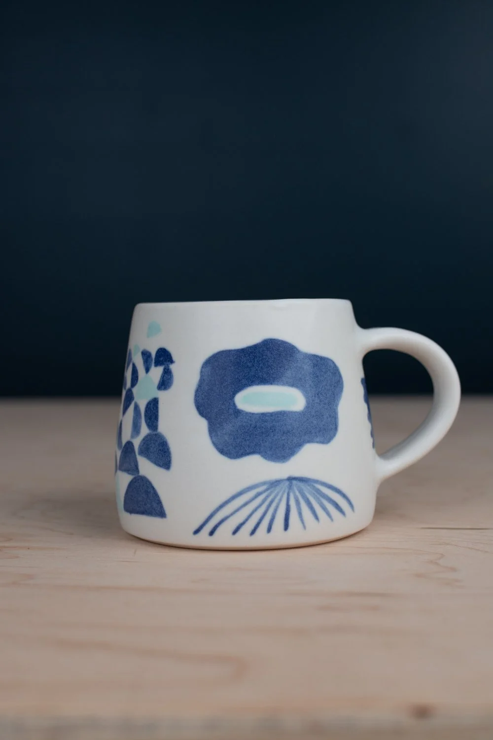 Hand-thrown porcelain mug with blue illustrations painted on the surface.