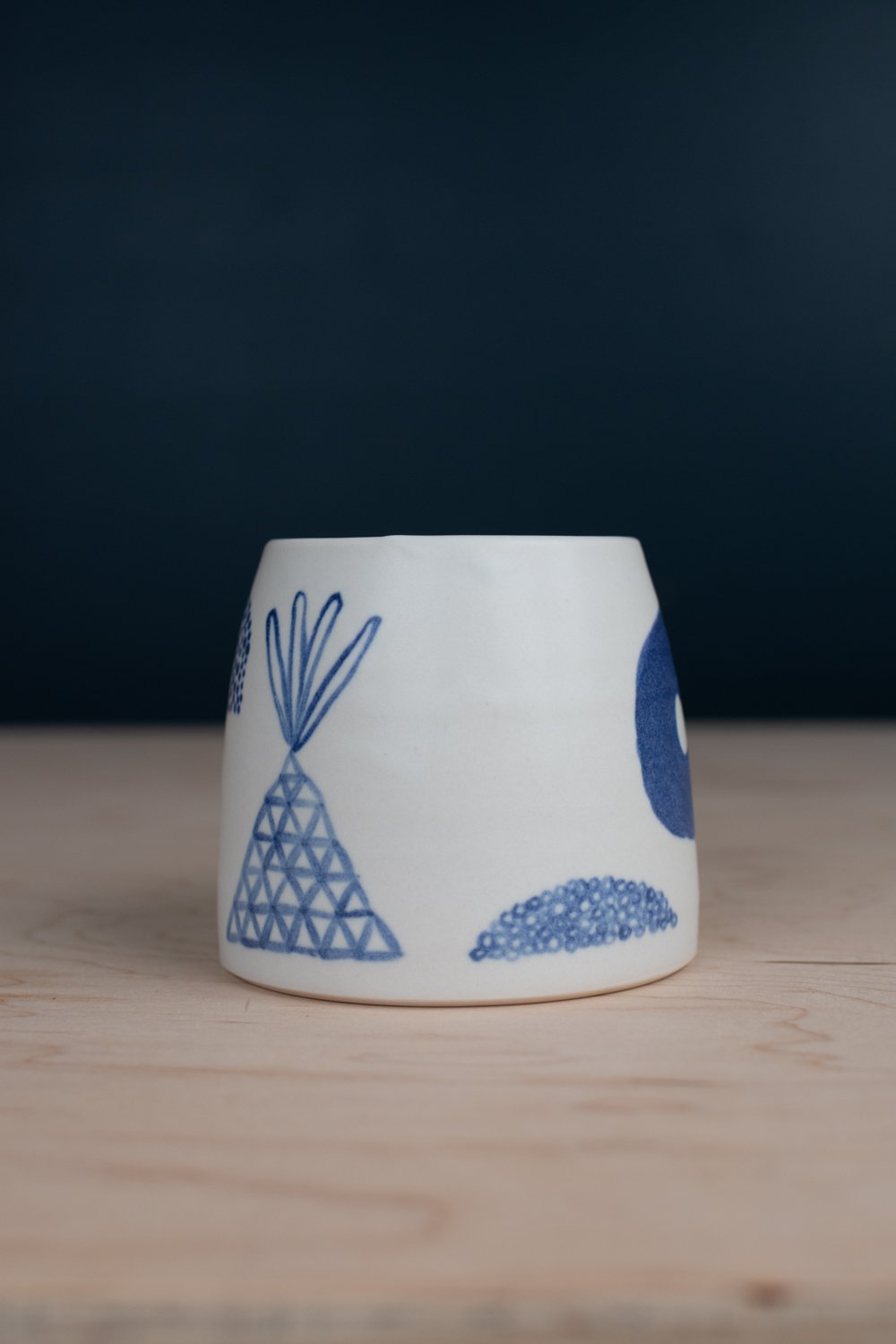Hand-thrown porcelain mug with blue illustrations painted on the surface.