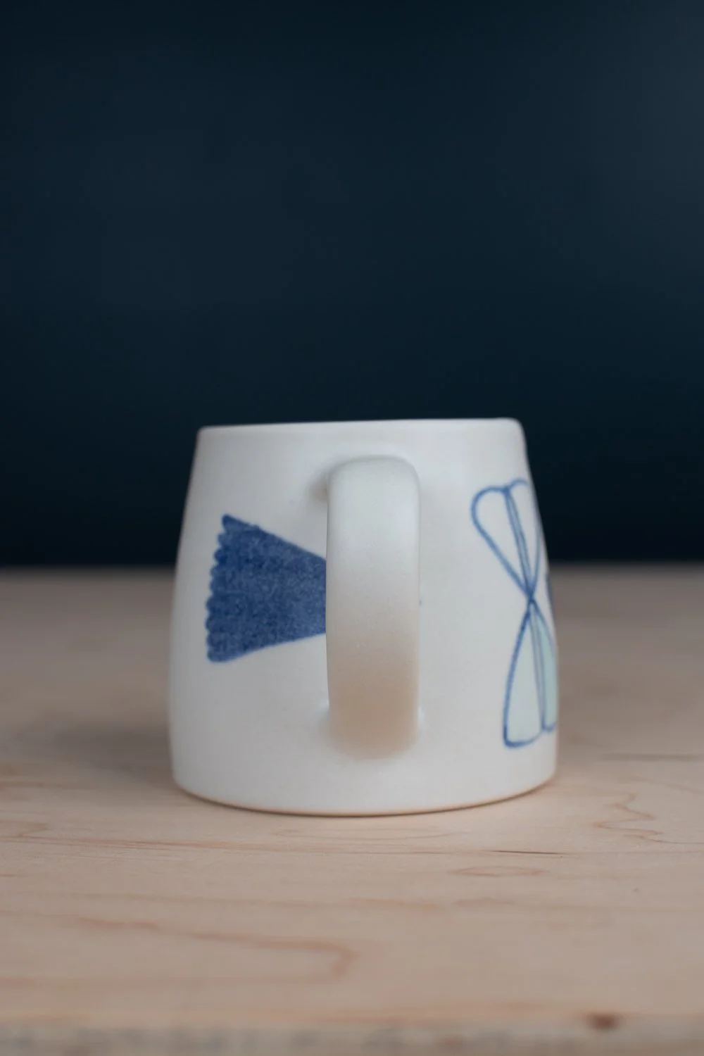 Hand-thrown porcelain mug with blue illustrations painted on the surface.