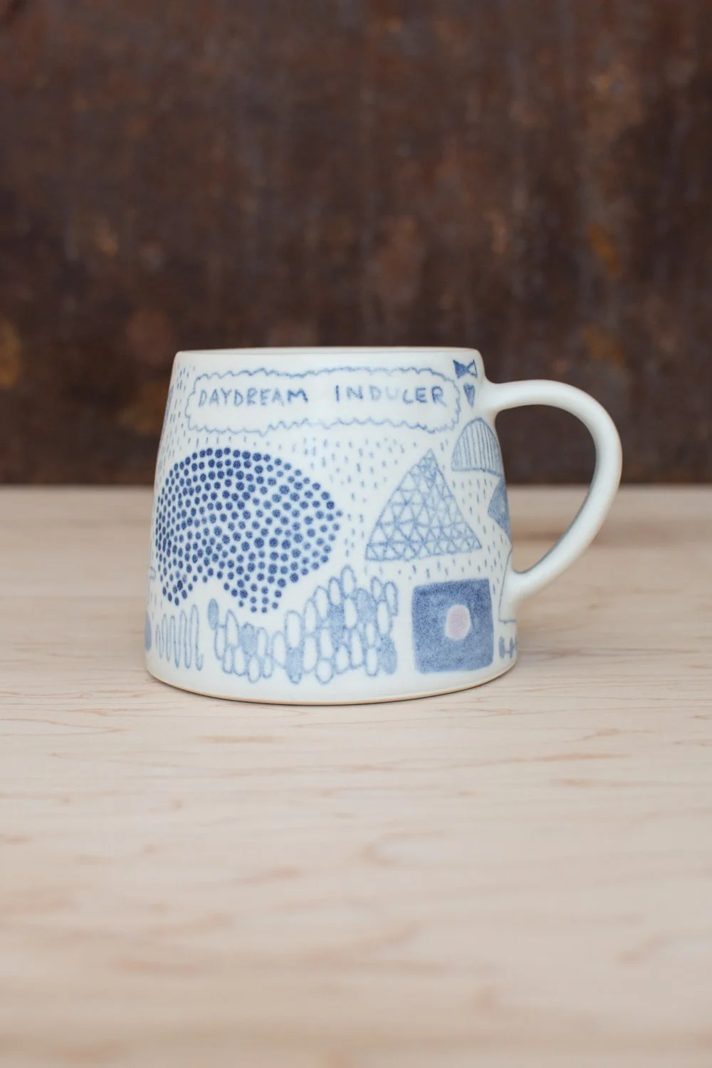 Hand-thrown porcelain mug with blue and purple illustrations painted on the surface.