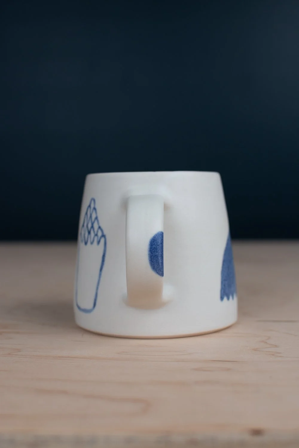 Hand-thrown porcelain mug with blue illustrations painted on the surface.