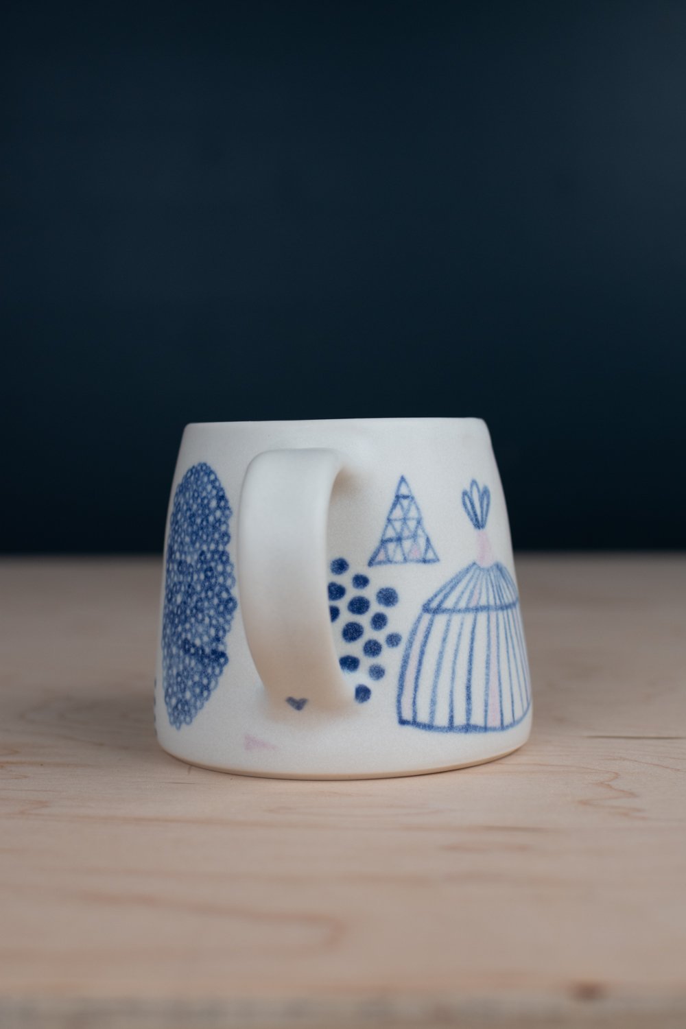 Hand-thrown porcelain mug with blue illustrations painted on the surface.