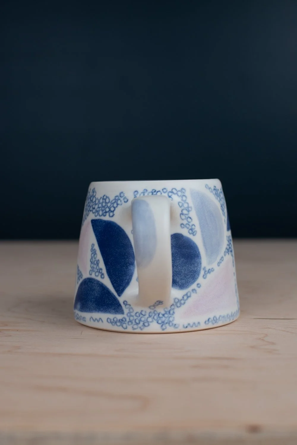 Hand-thrown porcelain mug with blue illustrations painted on the surface.