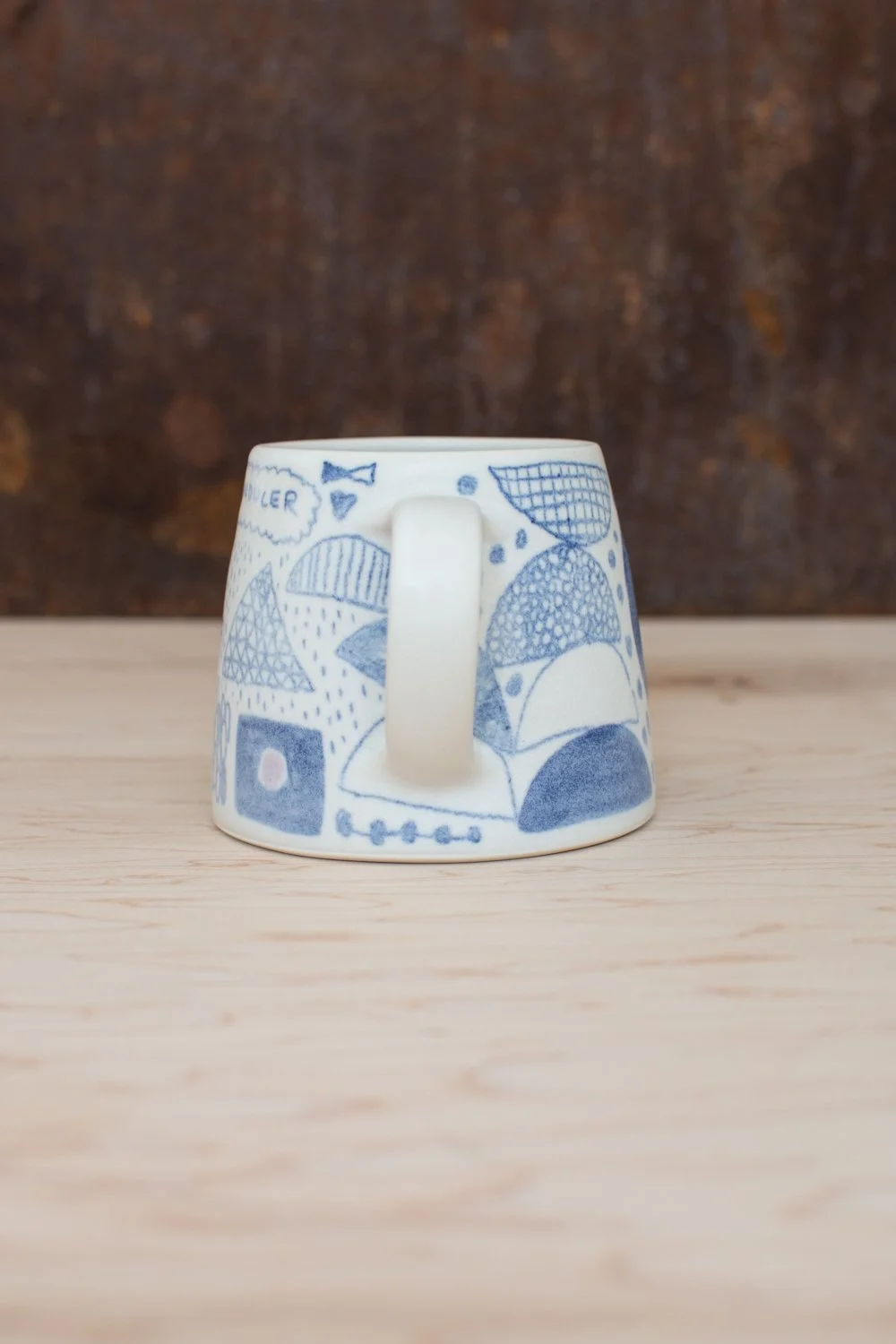 Hand-thrown porcelain mug with blue and purple illustrations painted on the surface.