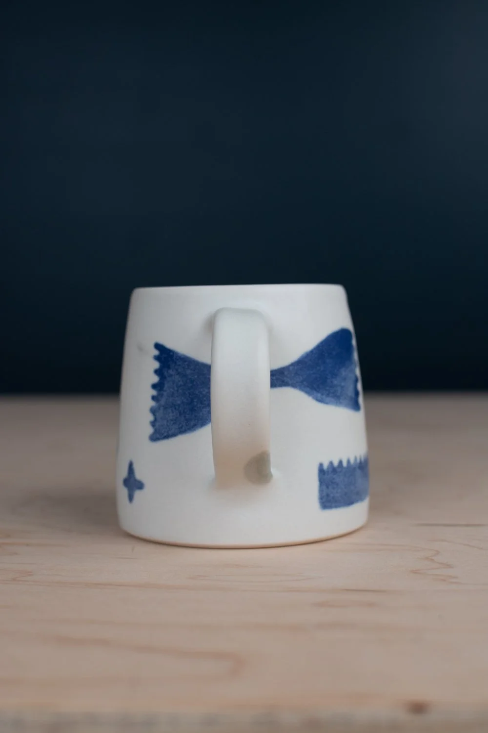 Hand-thrown porcelain mug with blue illustrations painted on the surface.