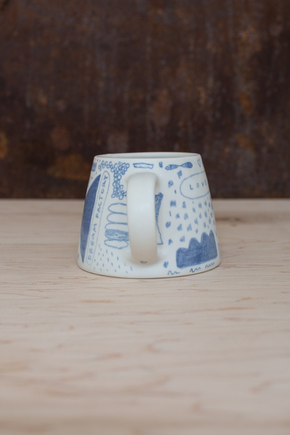 Hand-thrown porcelain mug with blue illustrations painted on the surface.
