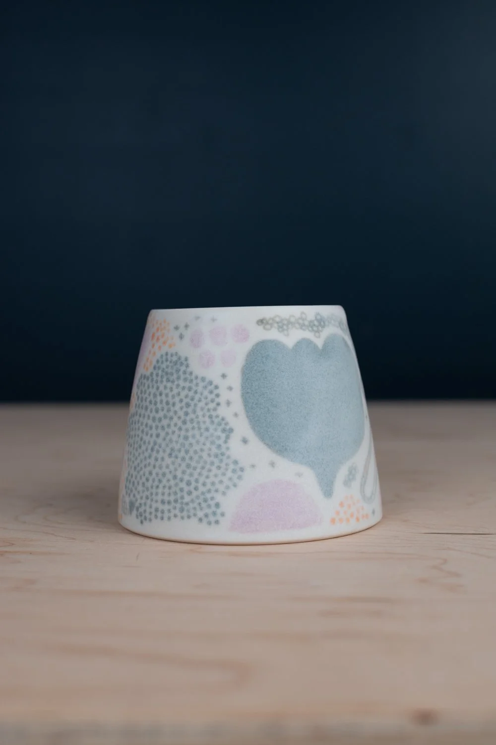 Hand-thrown porcelain mug with green, yellow, and lilac illustrations painted on the surface.
