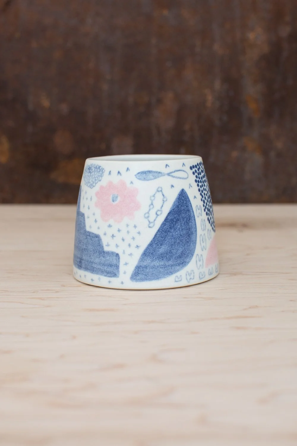 Hand-thrown porcelain mug with blue and pink illustrations painted on the surface.