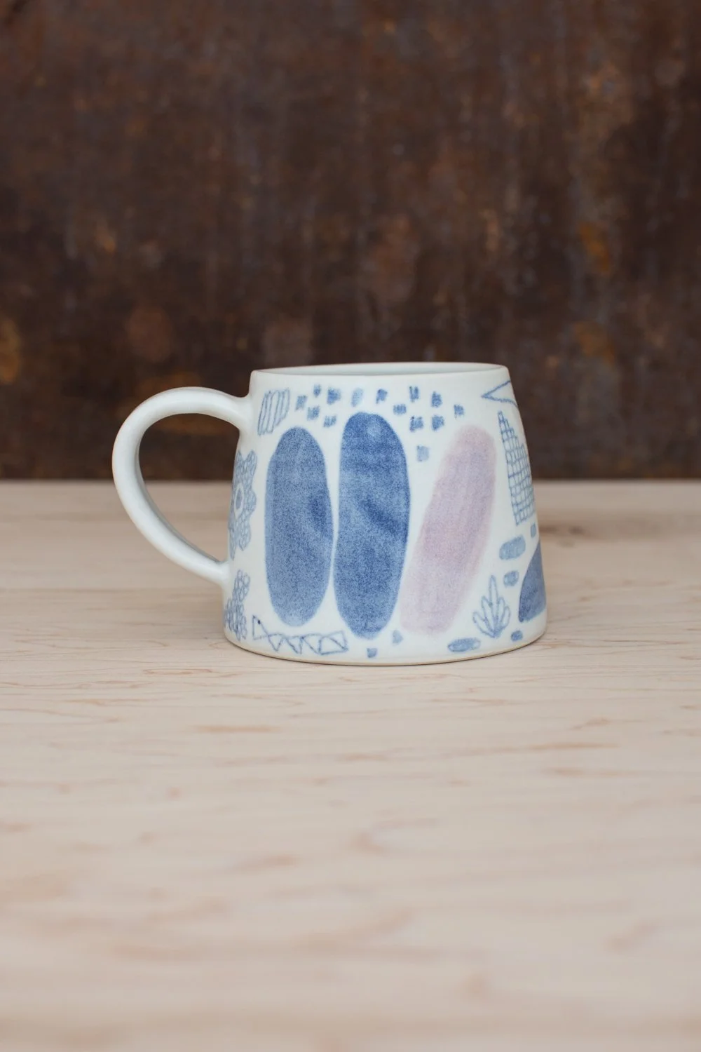 Hand-thrown porcelain mug with blue illustrations painted on the surface.