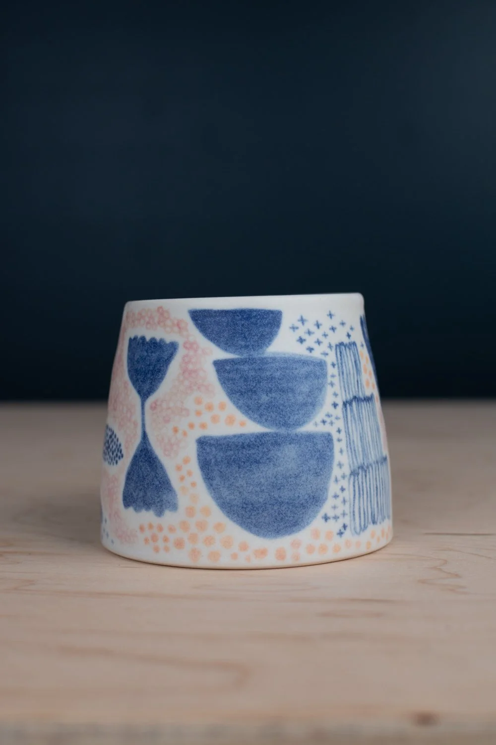 Hand-thrown porcelain mug with blue, blush, and tangerine illustrations painted on the surface.