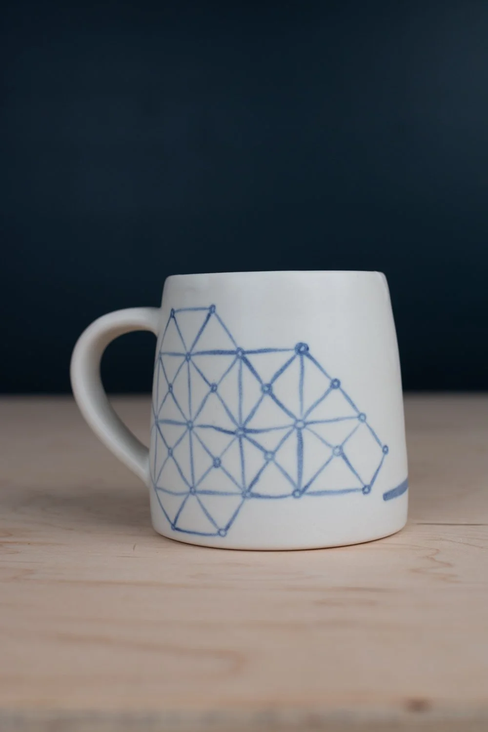 Hand-thrown porcelain mug with blue illustrations painted on the surface.