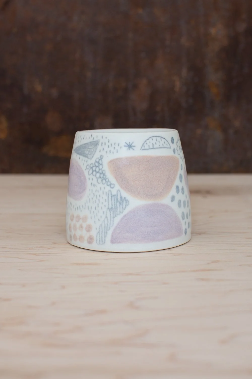 Hand-thrown porcelain mug with pink and ochre illustrations.