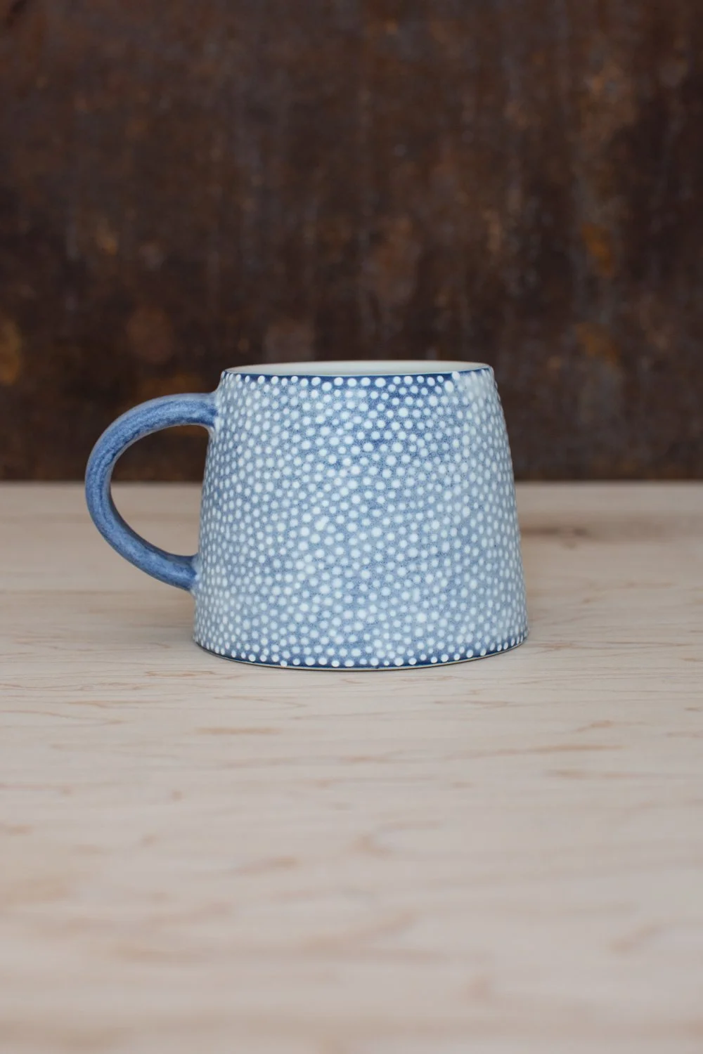 Hand-thrown porcelain mug with blue illustrations painted on the surface.