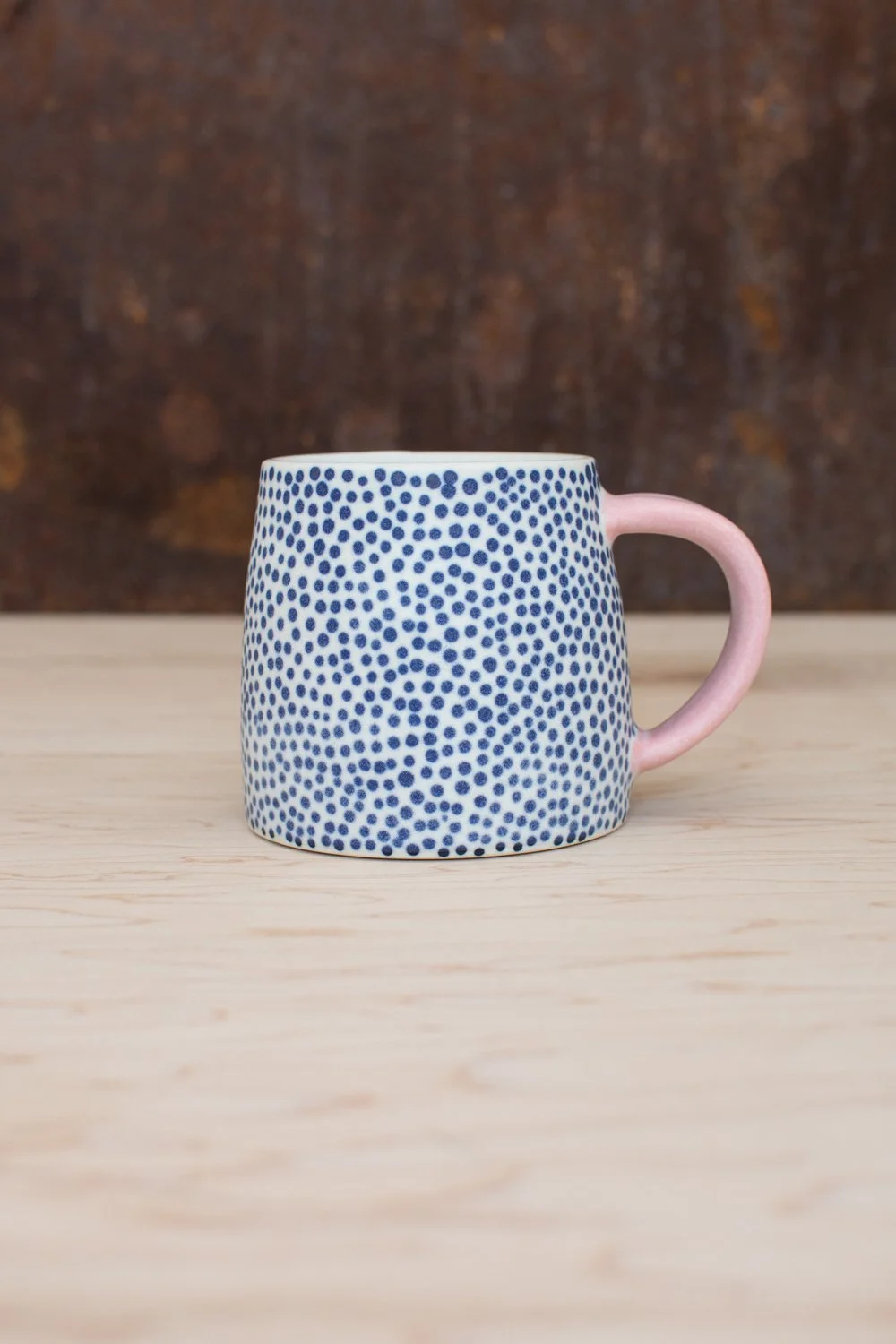 Hand-thrown porcelain mug with blue dots and a pink handle.