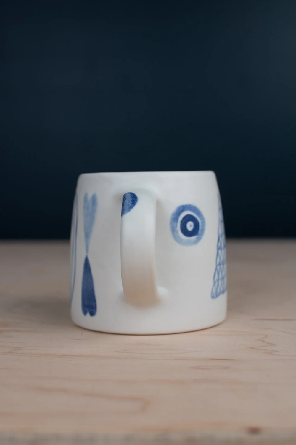 Hand-thrown porcelain mug with blue illustrations painted on the surface.