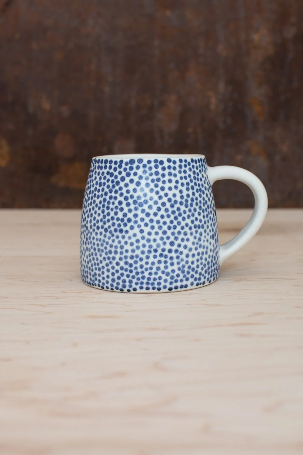Hand-thrown porcelain mug with blue dots painted on the surface.