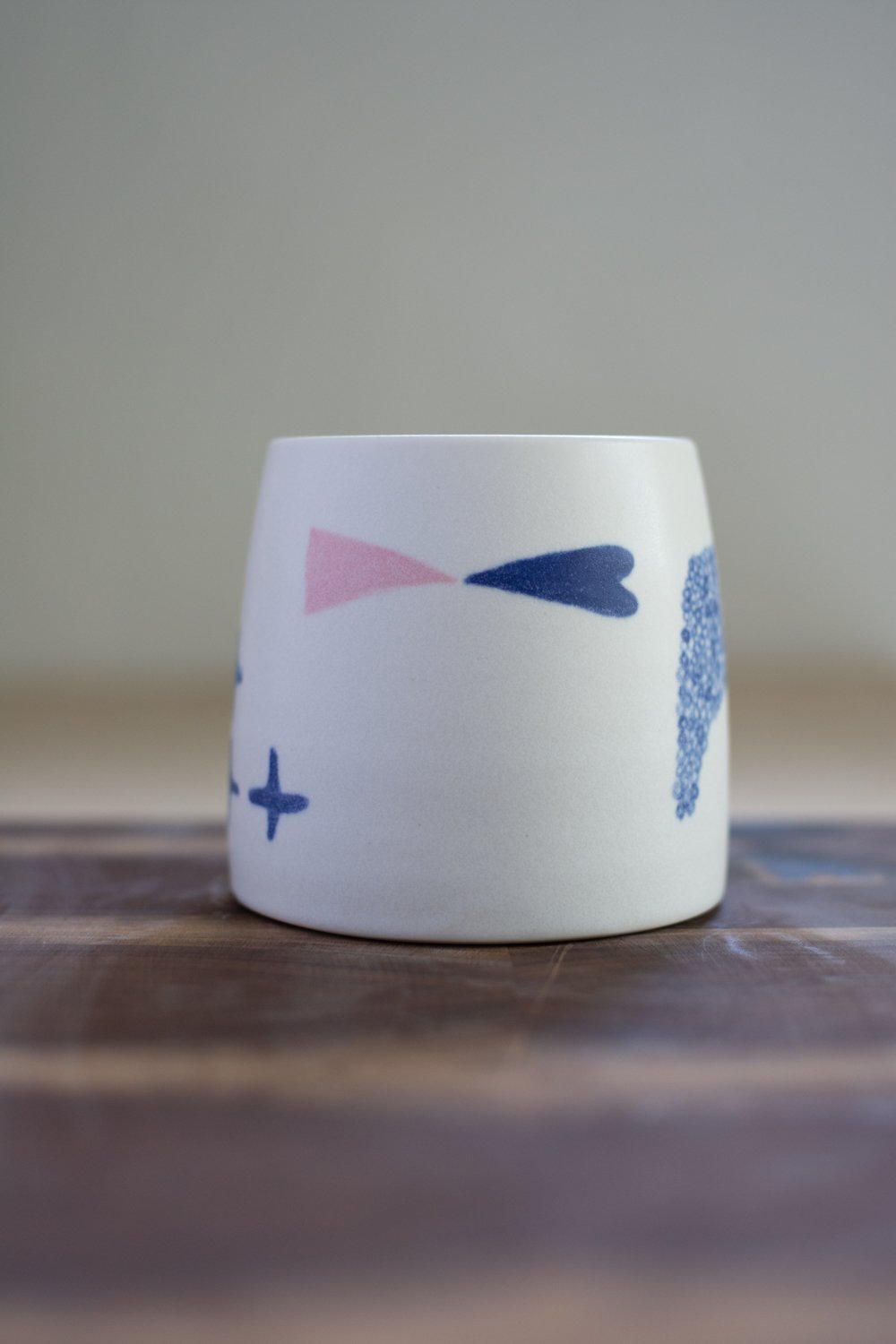 Hand-thrown porcelain mug with blue and pink illustrations painted on the surface.