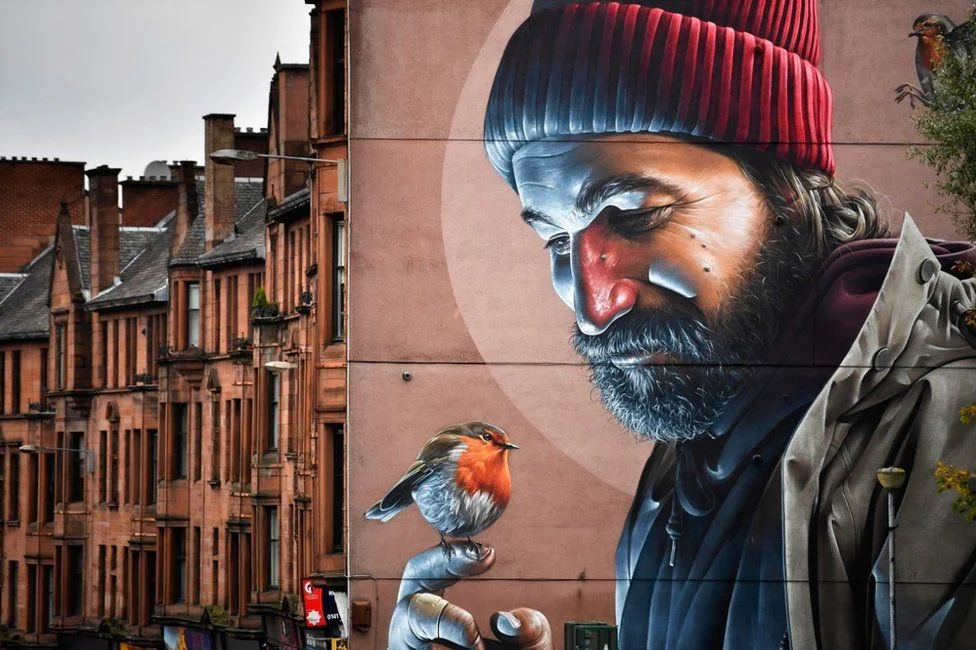 This mural depicts St Mungo, Glasgow's historic patron saint, in modern day clothes. The story goes that as a young boy he saved a bird that was being attacked by stones from a gang of youths, and brought it back to life. Source: http://www.telegraph.co.uk/travel/destinations/europe/united-kingdom/galleries/glasgow-s-new-street-art-trail-brightens-up-the-city/glasgow4/