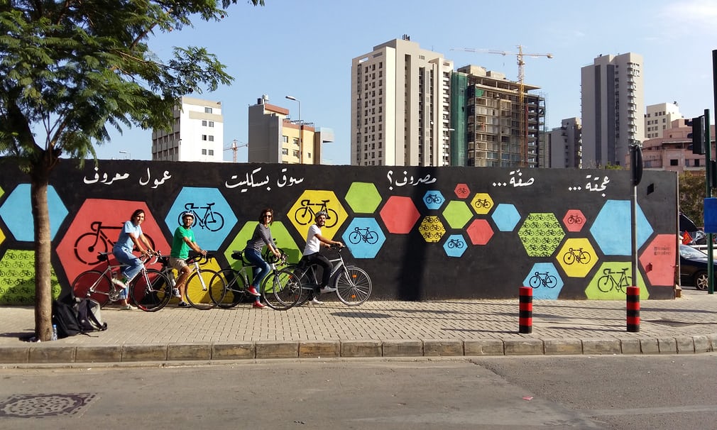 Members of The Chain Effect next to one of their 2016 murals in Beirut which reads "Traffic.. parking.. expenses.. ride a bicycle instead please!". Each painting is eye catching and encouraging with words that rhyme in Lebanese Arabic. Source: https://www.theguardian.com/cities/gallery/2017/jun/15/beirut-bike-street-art-chain-effect-in-pictures