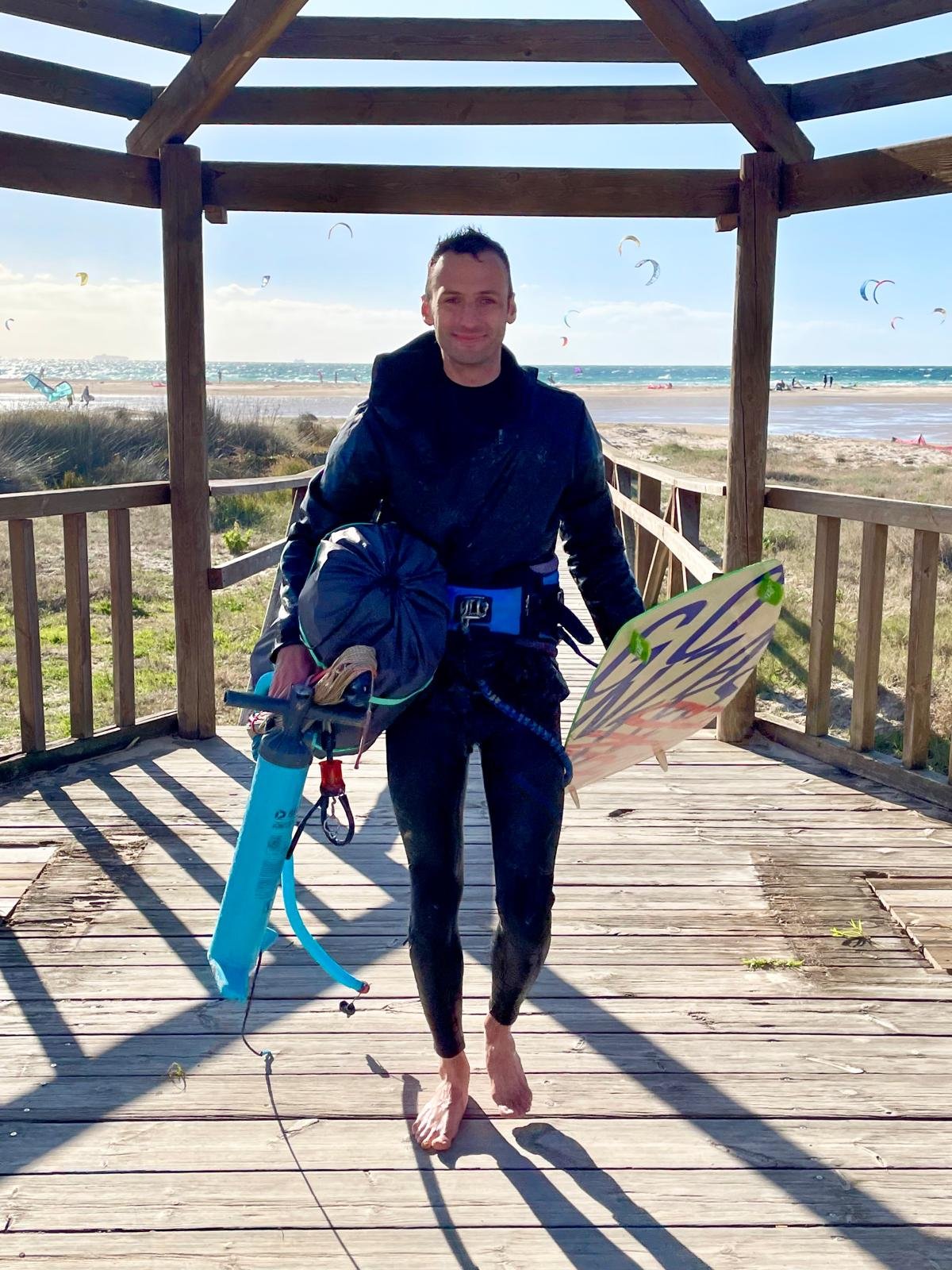 Chris Perren walking away from the beach carrying his kitesurfing equipment
