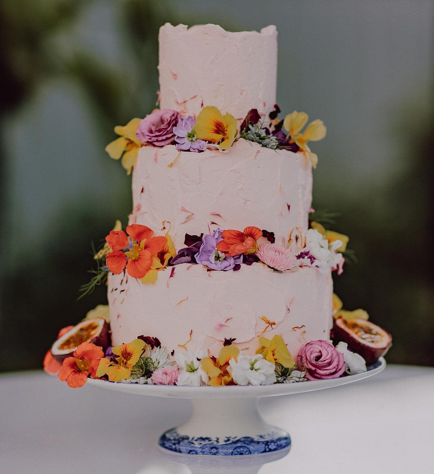 Well, here she is! My OWN WEDDING CAKE! I know you were probably expecting more, but let&rsquo;s be real, it was a backyard wedding for 20 I had to keep it under control. I just wanted a cake that was timeless, simple, fun and just looked delicious! But of course, the buttercream was pink, but a pastel pink. I smothered it in @piccolofarm edible flowers and home grown passionfruit. The bottom tier was a gluten free carrot cake, middle tier chocolate caramel crunch and top tier vanilla cake with passion fruit buttercream and raspberries. Photo by @juddric #wedding #weddingcake #edibleflowers