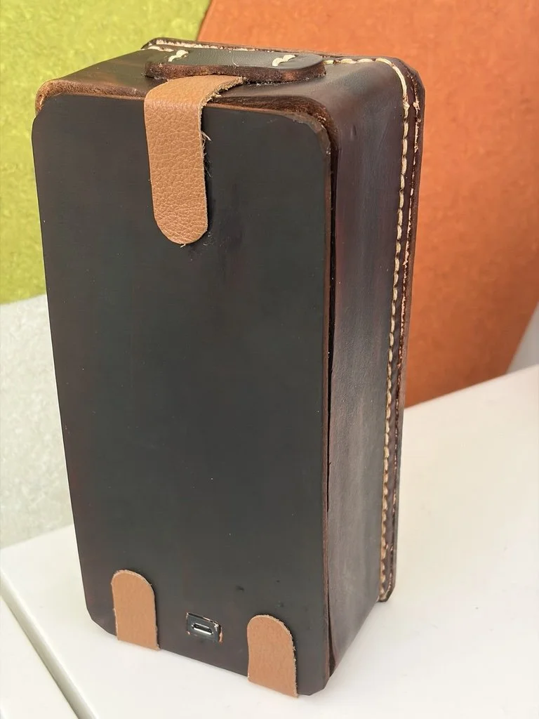 The rear view of a janky leather box with leather hinges, charge port, and leather strap closure. It is, if anything, even jankier than the front