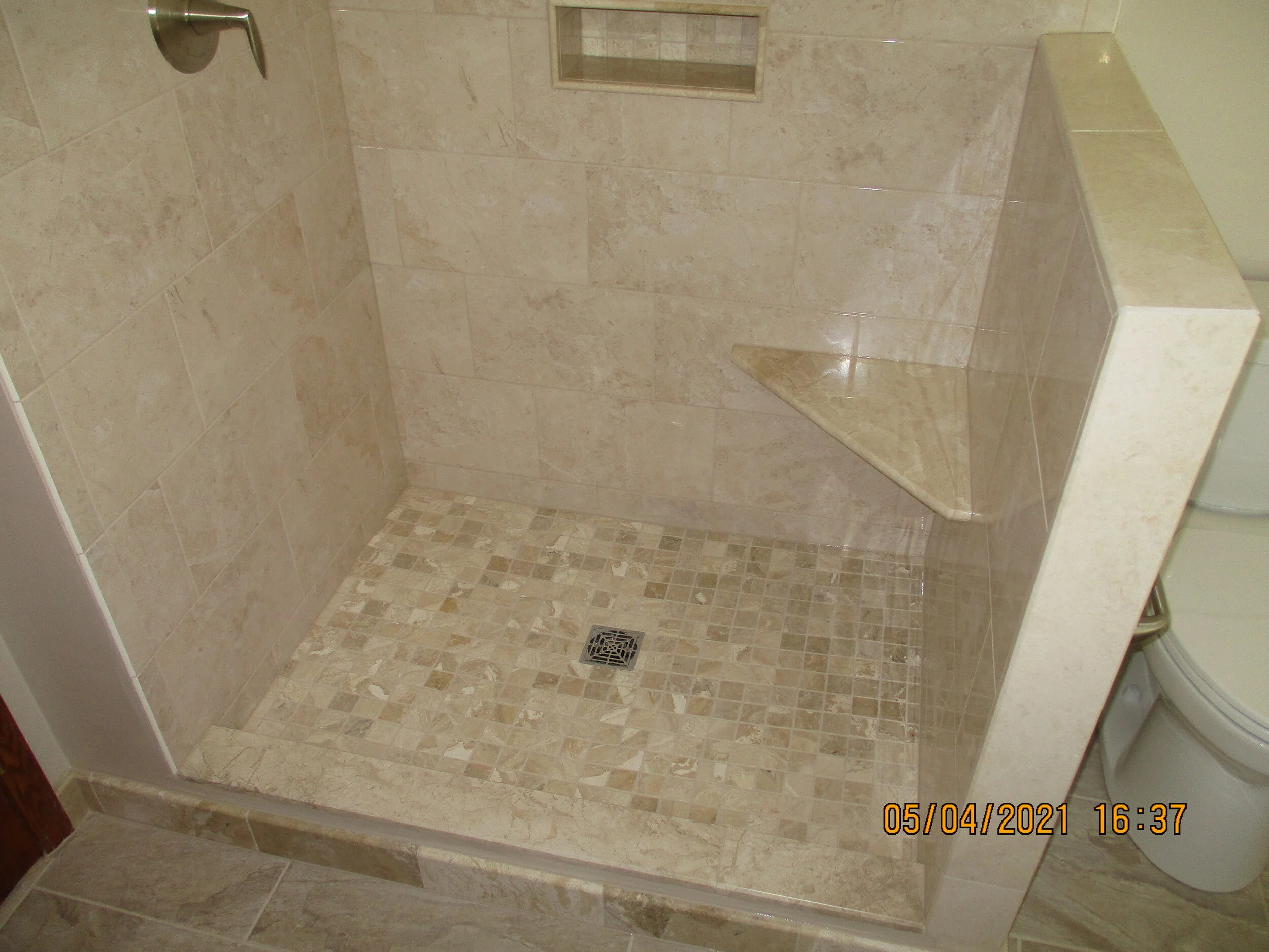 Custom shower pan with natural stone corner seat, recessed niche and ledge wall