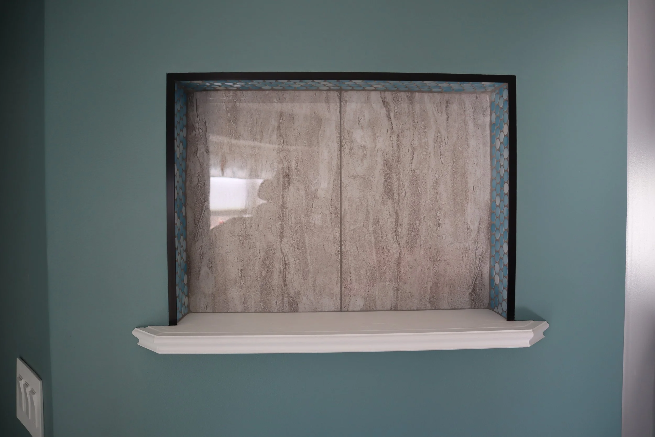 After: Foyer wall with recessed niche. India tile in the back with blue penny tile on the sides and top. Trimmed with a black metal edging and wood base on the bottom.