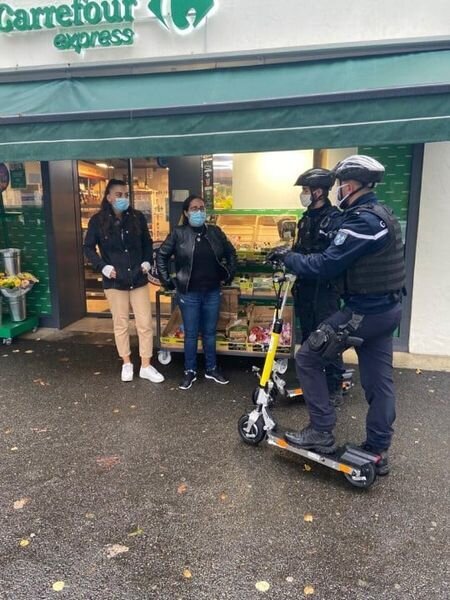 Two French Police Officers on Electric Scooters talking with the public Outside a Shop.