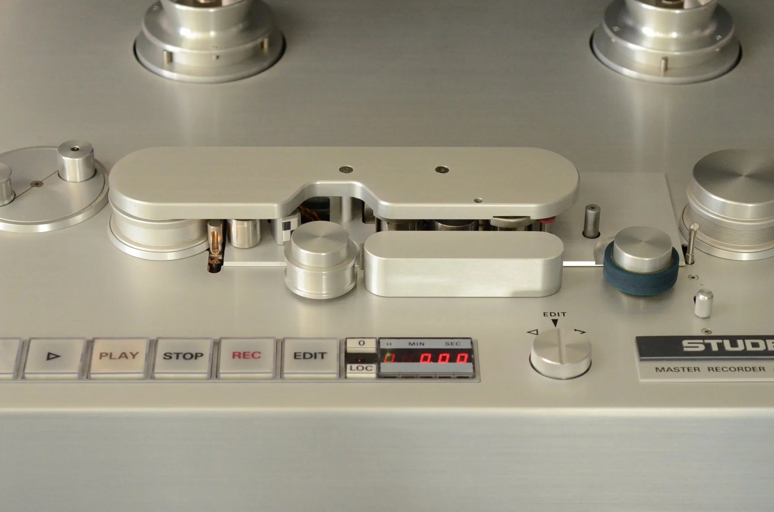 Close-up of a vintage reel-to-reel tape recorder with metallic knobs and buttons, including play, stop, record, and edit functions.