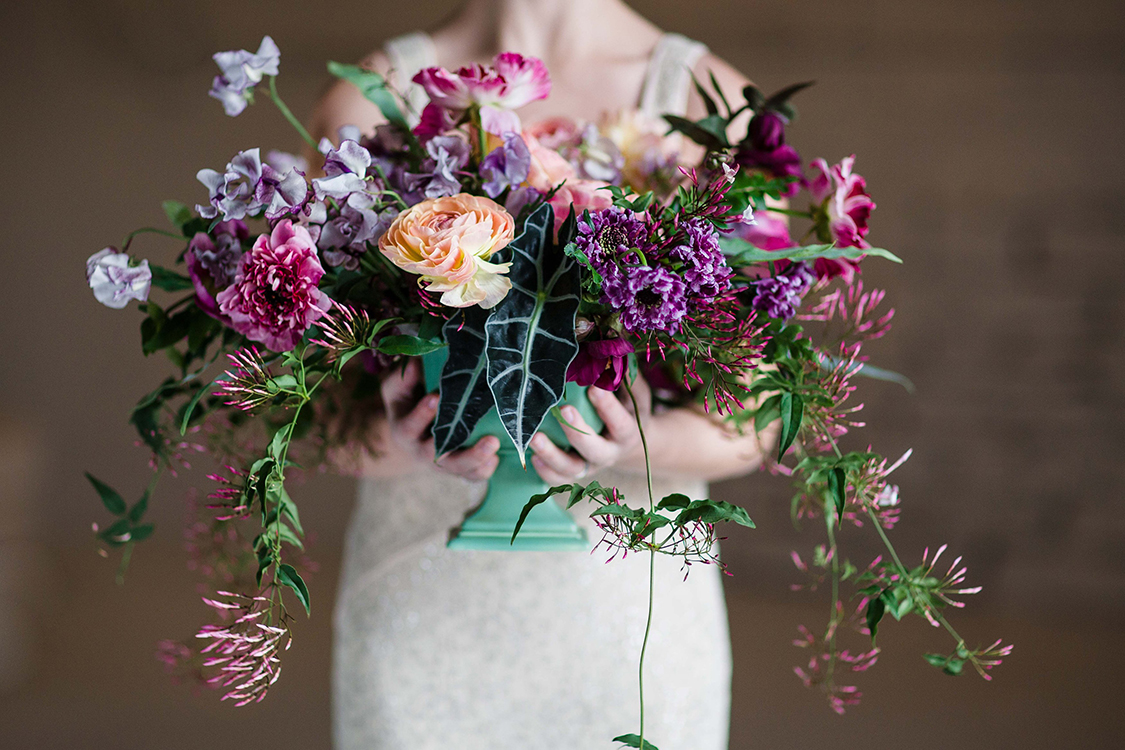  Overflowing centerpiece with purple Japanese scabiosa, purple hellebores, Silvery Moon Japanese sweet pea, Charlotte ranunculus, peach ranunculus, jasmine vine, blue star fern and Alocasia ‘Polly’, in a vintage mint footed bowl. &nbsp;Image by&nbsp;